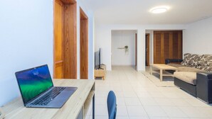 Una sala de estar moderna con una computadora portátil sobre un escritorio de madera, un sofá y un televisor.