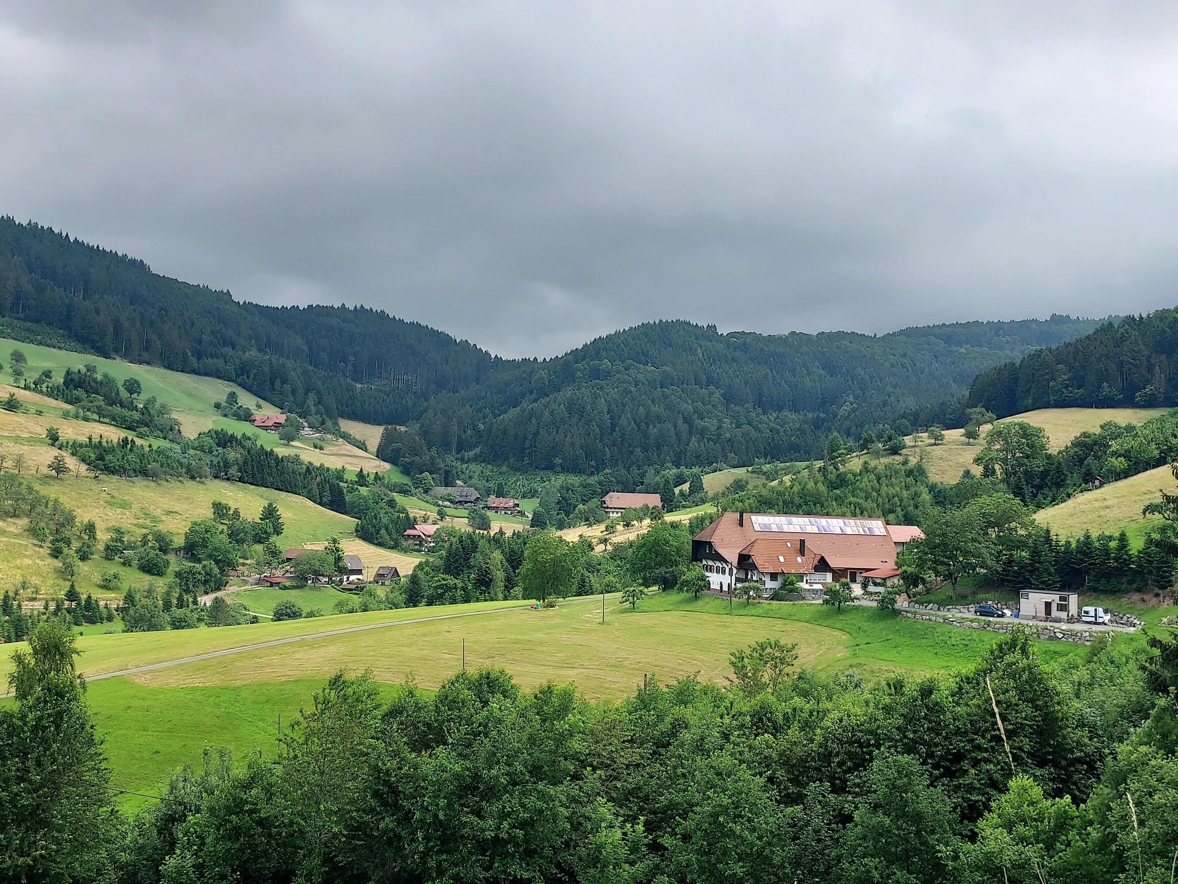 Un paysage rural caractérisé par des collines douces, des maisons dispersées et de vastes forêts.