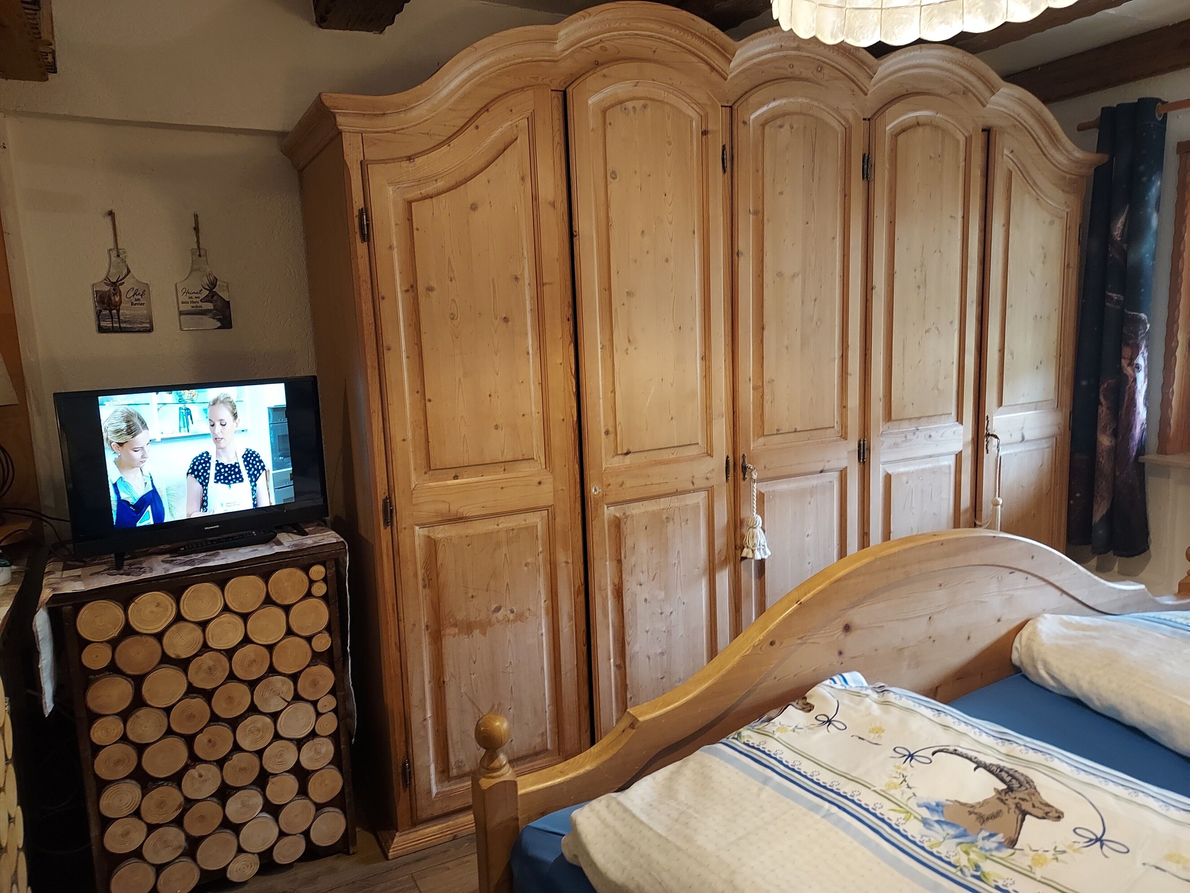 A bedroom with a wooden wardrobe, a television on a wooden stand, and a bed with a floral bedspread.