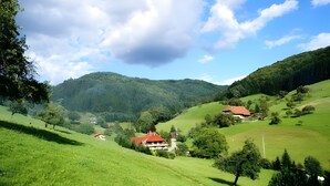 A rural landscape with rolling hills, a few scattered houses, and a clear sky.