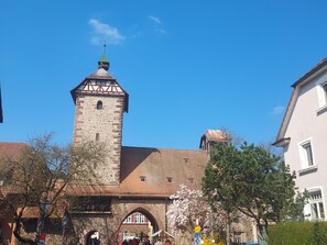 Ein historischer Stein-Turm mit grüner Spitze, einem Bogenportal und einem strahlend blauen Himmel.