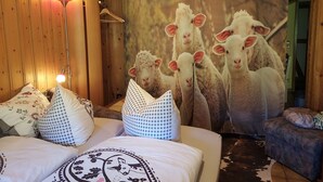 A bedroom with a bed, pillows, a lamp, a curtain with a sheep print, and a sofa.