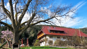 A two-story building with a red-tiled roof, a large tree in the foreground, and a playground with swings and slides.