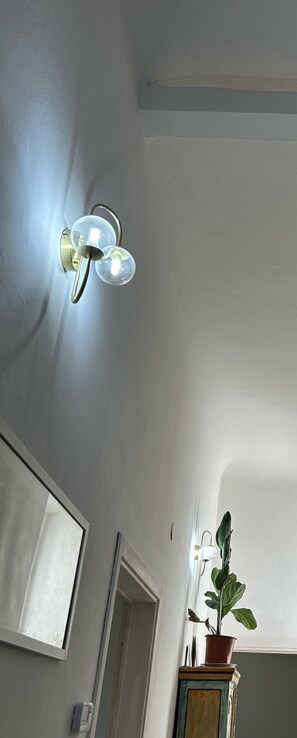 Een plafondlamp met drie lampen, een plant in een pot op een kastje, en een deur met een raam.