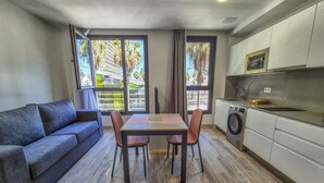 A compact living space with a sofa, dining table, chairs, a washing machine, and a kitchen area. - Beachfront Apartment in Las Palmas Near Playa (Las Palmas de Gran Canaria)