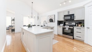 A modern kitchen with white cabinetry, a central island, stainless steel appliances, and a pendant light. - Ellerslie - Sleeps 6 - AC - Garage (Edmonton)