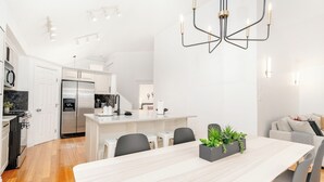 A modern kitchen with white cabinets, a stainless steel refrigerator, and a dining area with a white table and chairs. - Ellerslie - Sleeps 6 - AC - Garage (Edmonton)