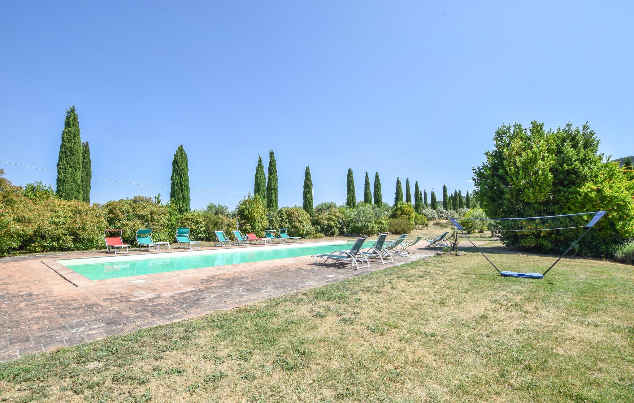 Une piscine entourée de chaises longues et d’un hamac, le tout bordé de grands arbres et de verdure.