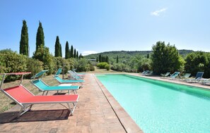 Piscina com espreguiçadeiras e vista para árvores e colinas.