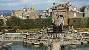 Un edificio histórico con una fuente central, rodeado por un jardín formal y una masa de agua.