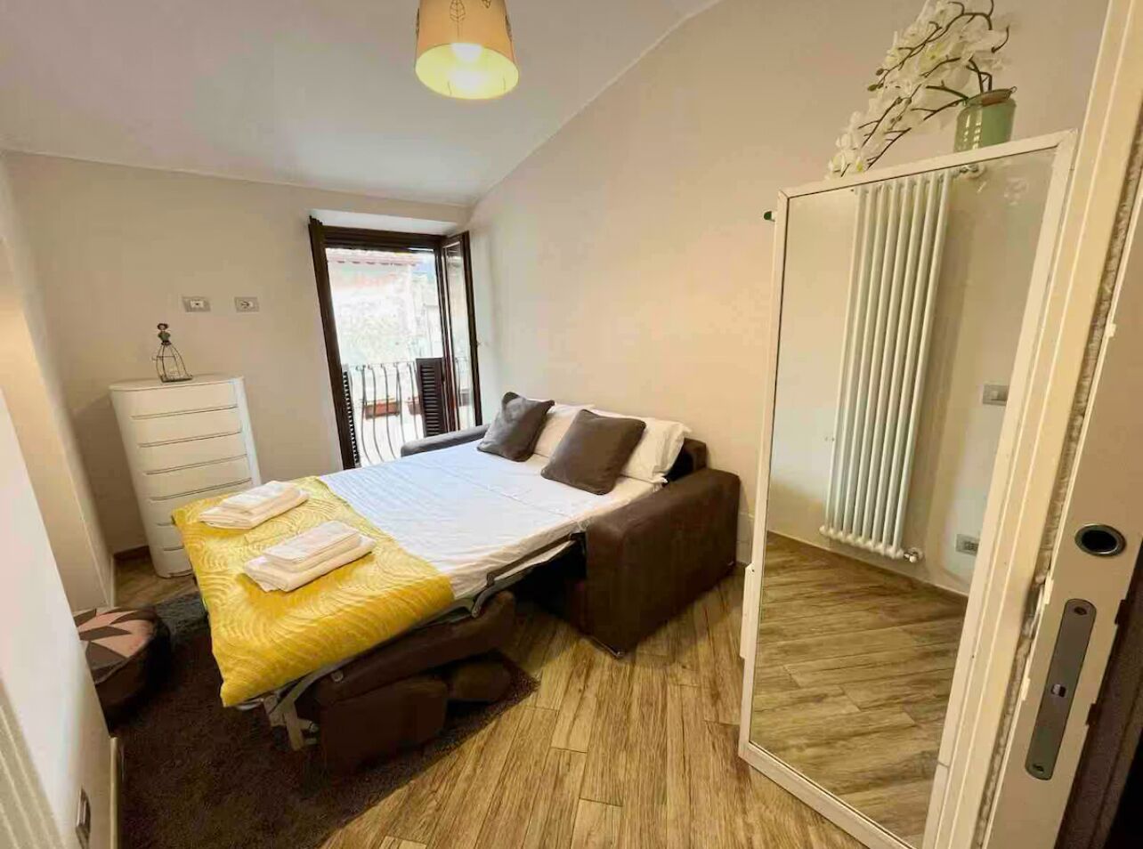 A bedroom with a bed, a chest of drawers, a radiator, and a door leading to a balcony.
