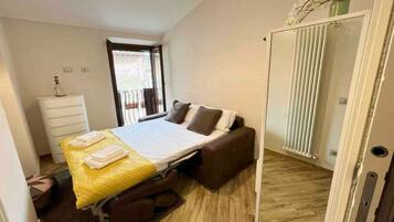 A bedroom with a bed, a chest of drawers, a radiator, and a door leading to a balcony.