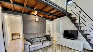 Una sala de estar moderna con un sofá gris, un televisor de pantalla plana sobre un mueble blanco y una escalera de madera.