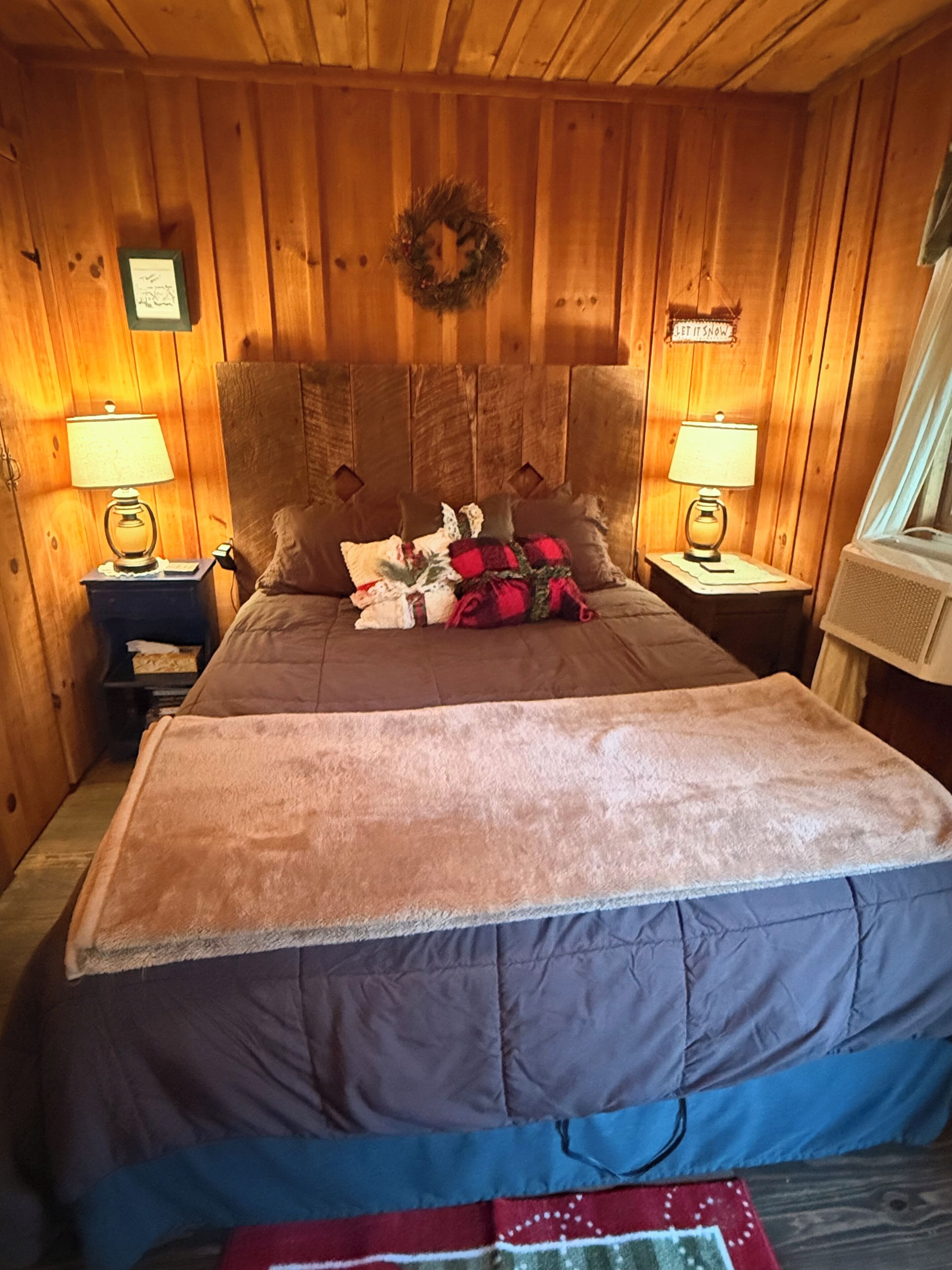 A cozy wooden cabin bedroom with a bed, two nightstands, and a window.