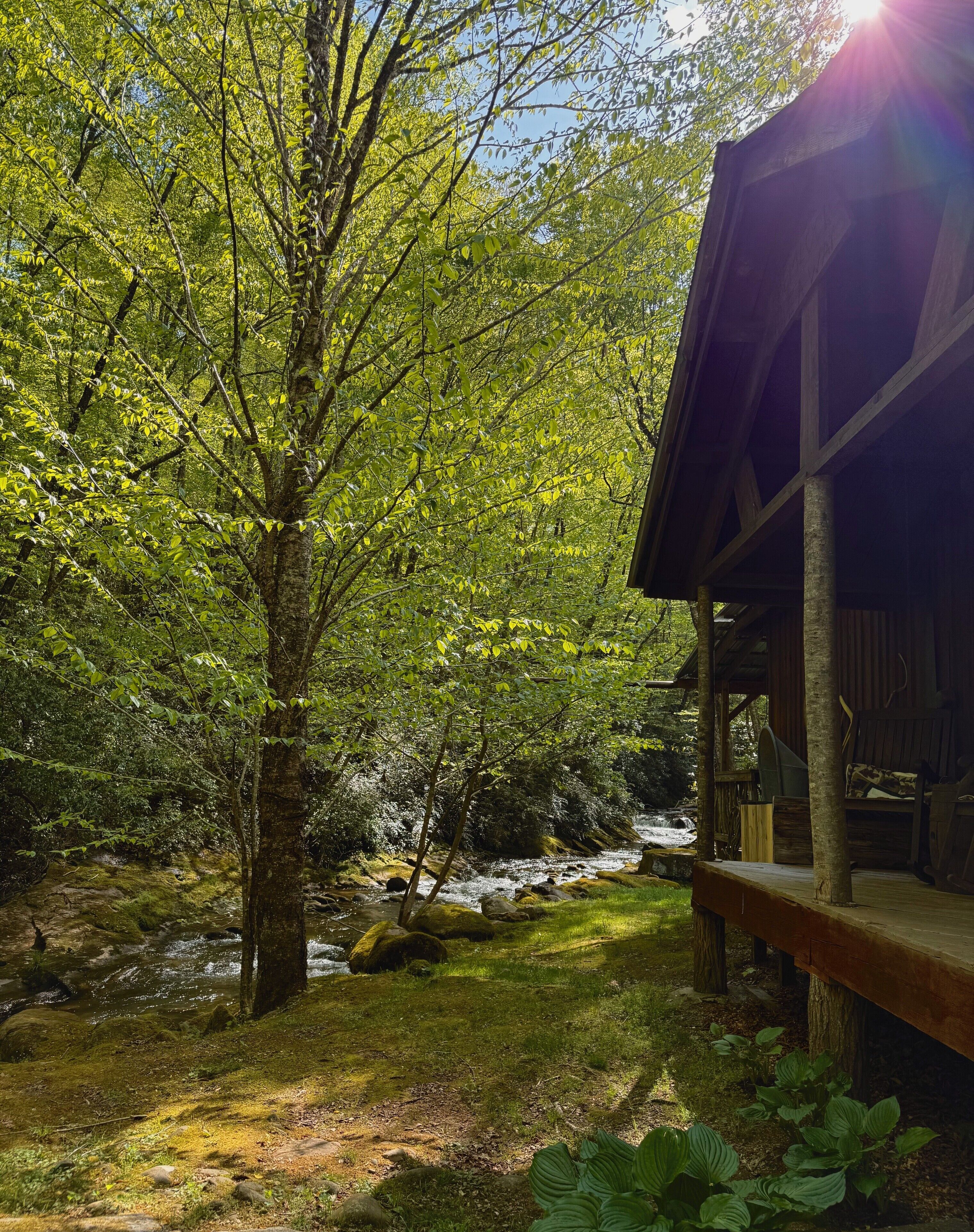 A rustic cabin with a wooden deck and a view of a flowing stream.