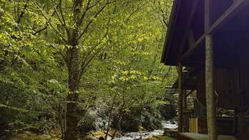 A rustic cabin with a wooden deck and a view of a flowing stream.