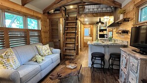 L’intérieur d’un chalet rustique, avec un plafond en bois, un canapé, une table basse, un coin cuisine et un escalier.