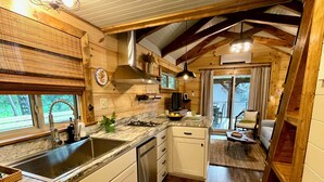 Une cuisine rustique aménagée dans une cabane en bois, avec un évier, une cuisinière et des placards. Un coin repas est également prévu, avec une table et des chaises.