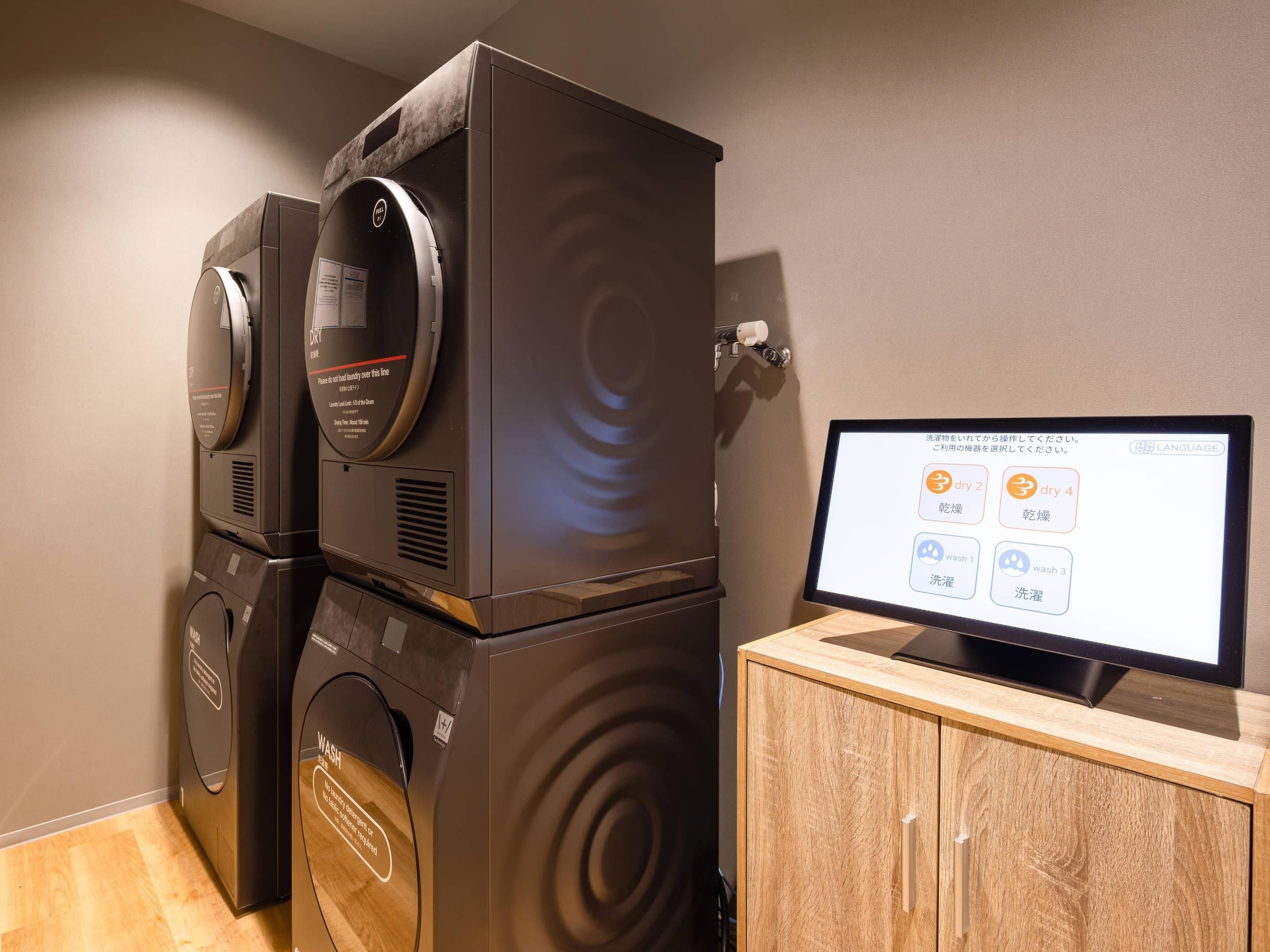 A modern laundry room with stacked washing machines and dryers, a digital display for selecting wash cycles, and a wooden cabinet.