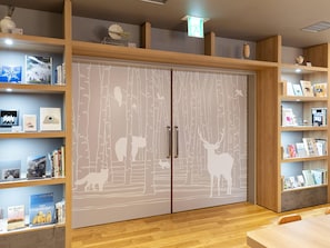 Quarto com um guarda-roupa amplo de design inspirado na floresta, prateleiras de madeira com livros e objetos decorativos, e uma mesa de madeira.