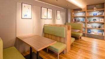 A modern library with wooden tables and green cushioned seating, featuring bookshelves with various books and framed artwork on the walls.