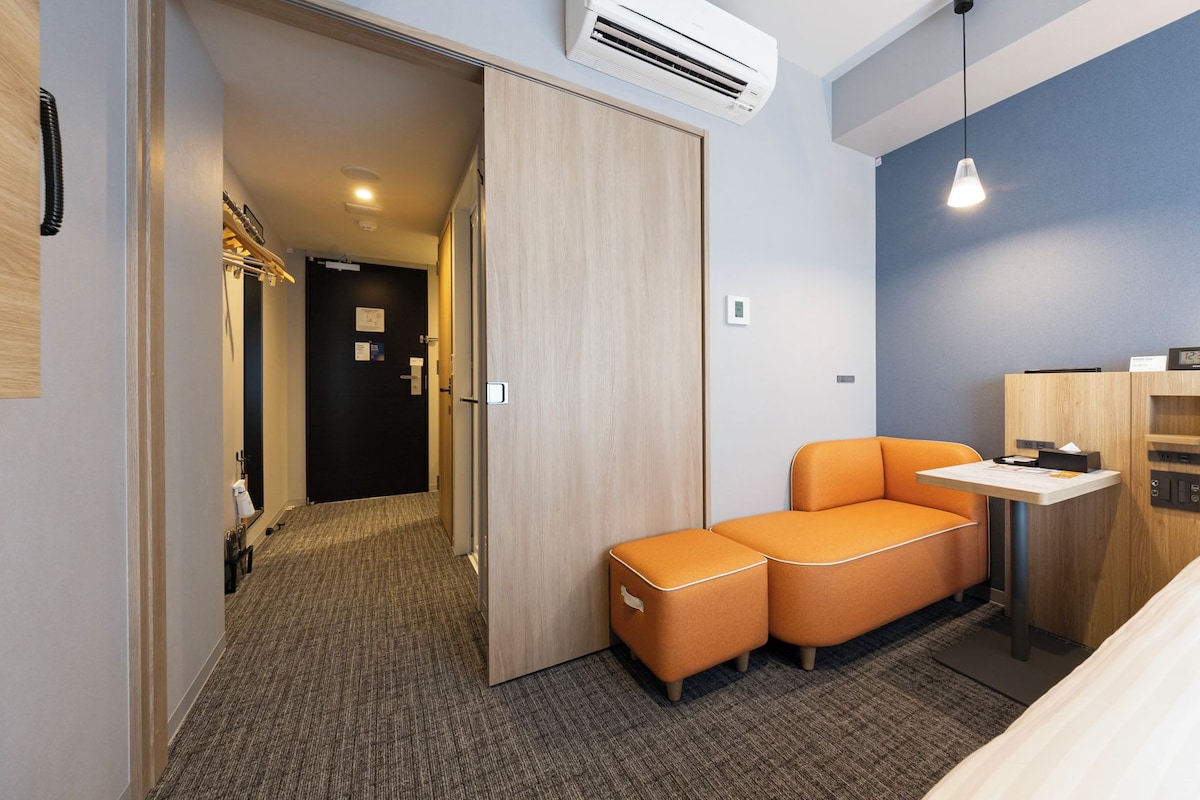 Una habitación de hotel con cama, escritorio, sofá naranja y armario.