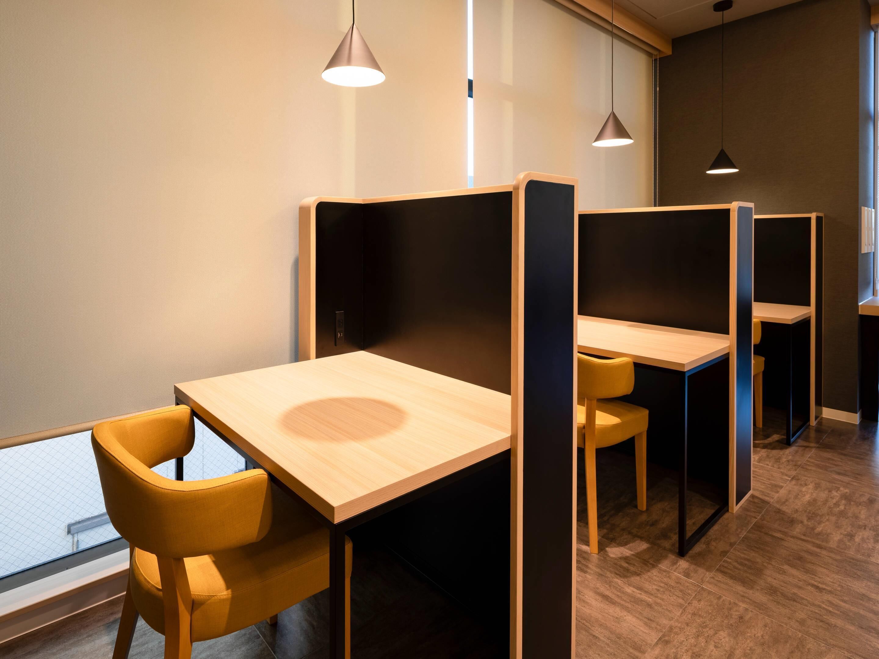 A modern office space with partitioned workstations, each with a wooden table and a yellow chair.