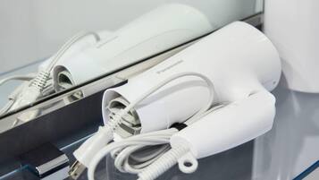 A white hair dryer and its charging cable on a reflective surface.