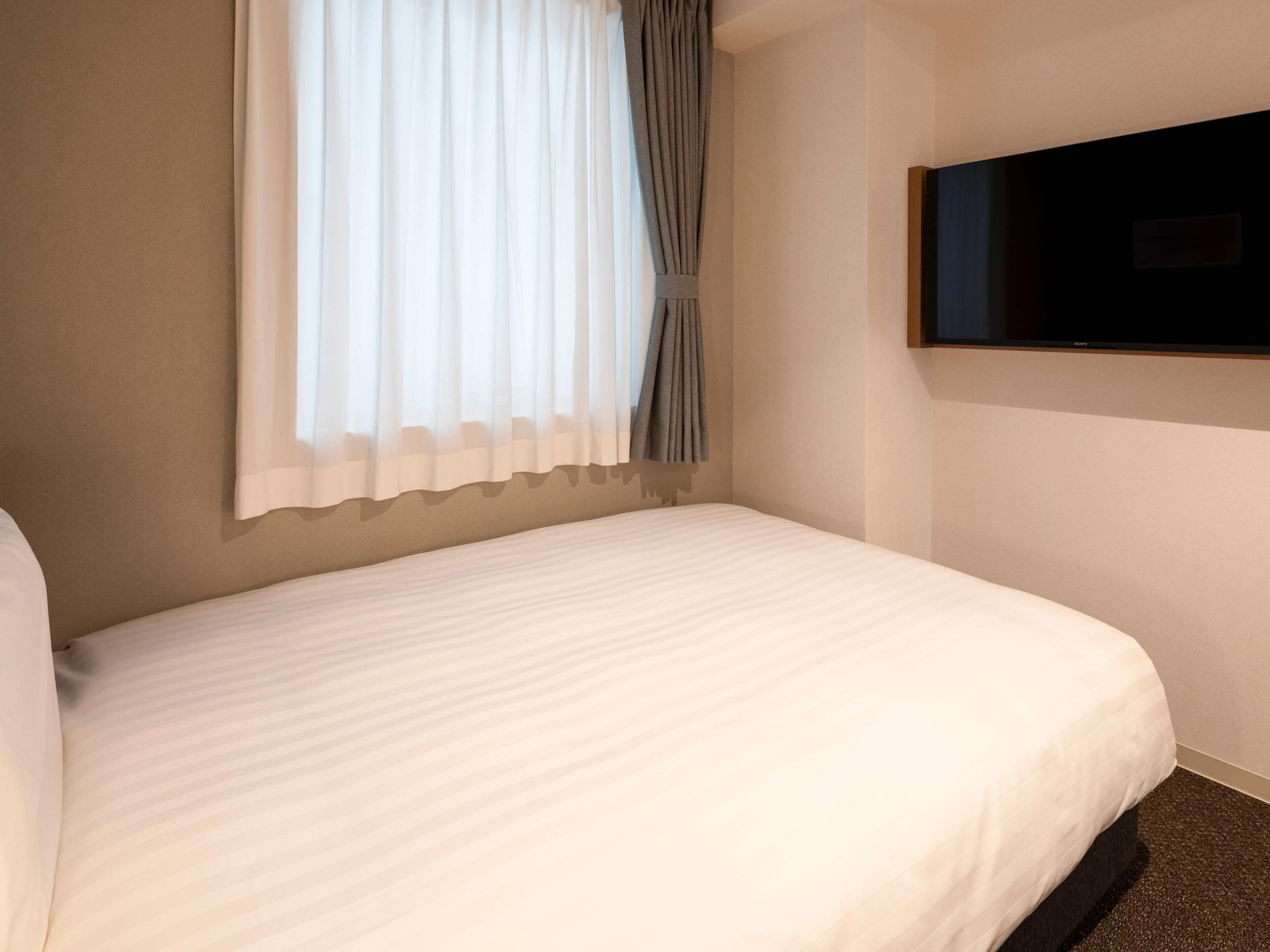 Habitación de hotel con una cama, un televisor de pantalla plana montado en la pared y un ventanal con cortinas.