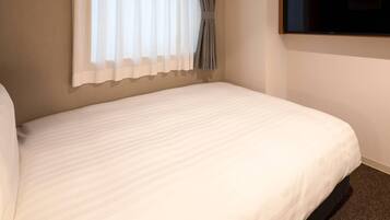 Habitación de hotel con una cama, un televisor de pantalla plana montado en la pared y un ventanal con cortinas.