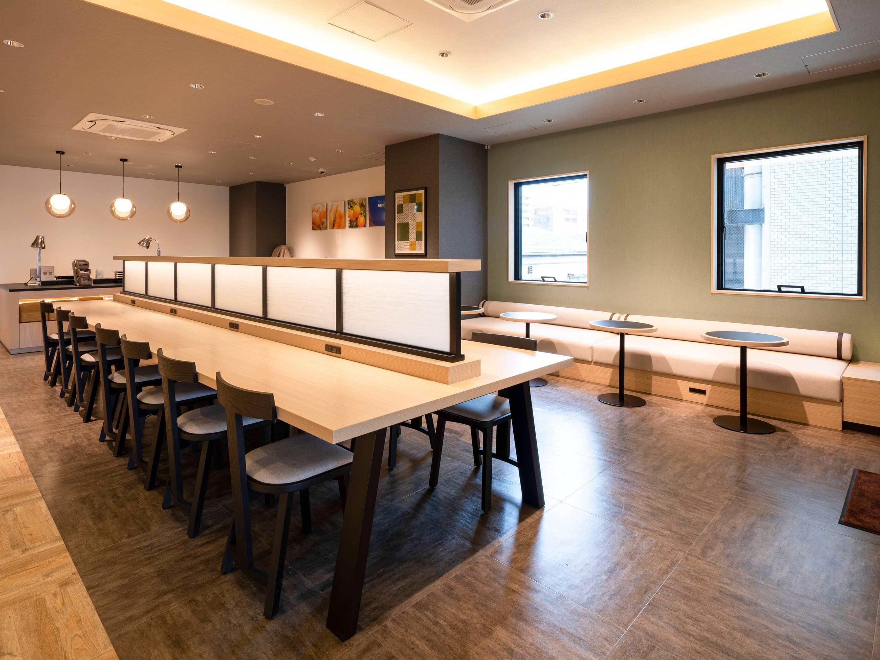 Un restaurante moderno con una larga mesa compartida, cabinas individuales y una zona de estar con vista a la ciudad.