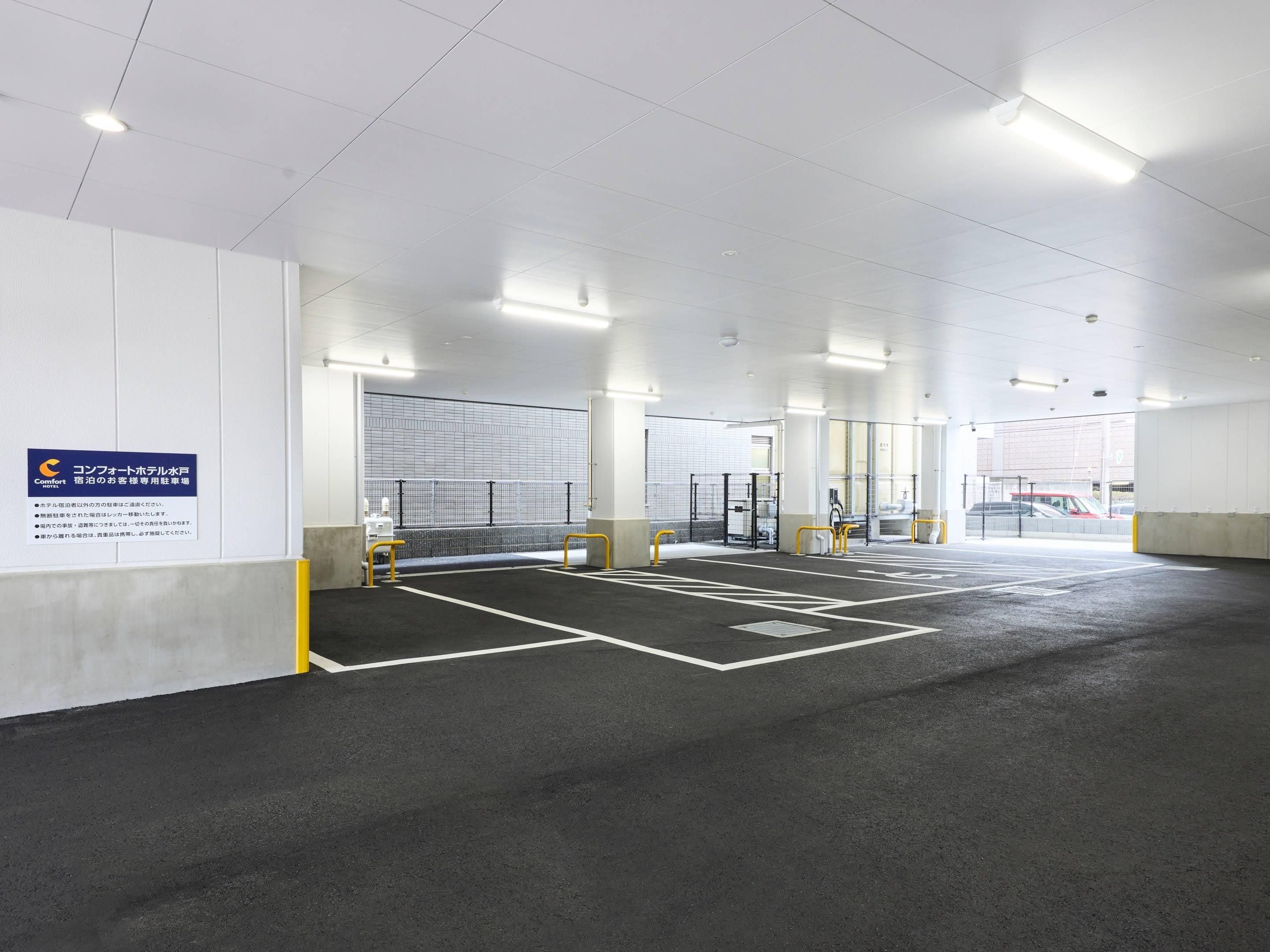 Uma área de estacionamento interna ampla, com vagas demarcadas, um portão de segurança e uma placa indicando que pertence a um hotel.