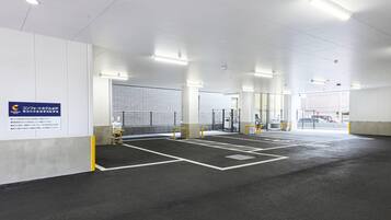 Uma área de estacionamento interna ampla, com vagas demarcadas, um portão de segurança e uma placa indicando que pertence a um hotel.