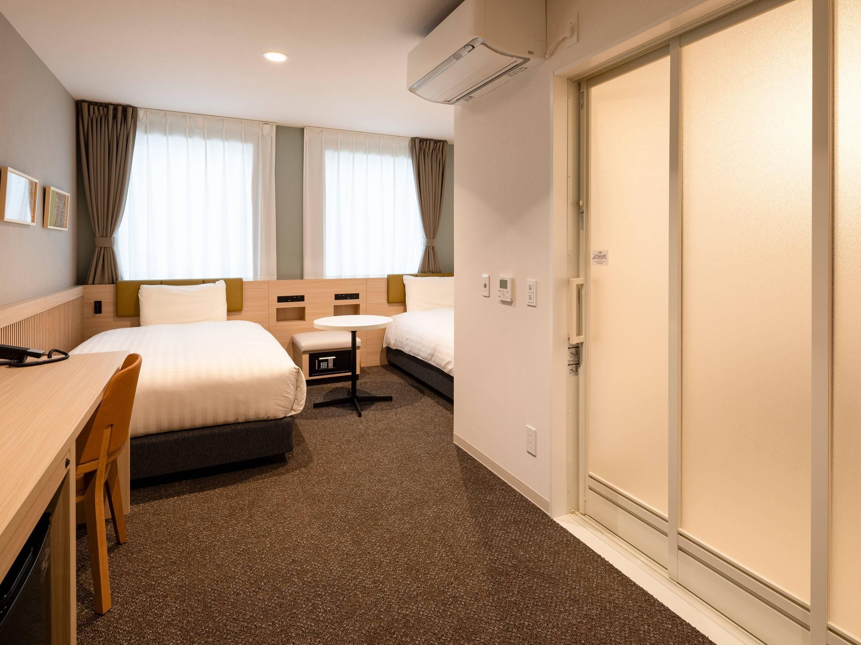 A hotel room with two beds, a desk, a chair, a small table, and a wardrobe.
