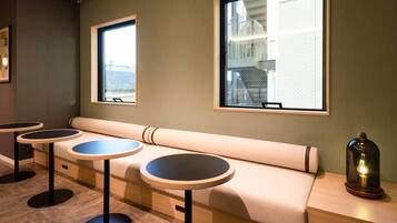 A seating area with a bench and three round tables, large windows, and a lamp on a side table.