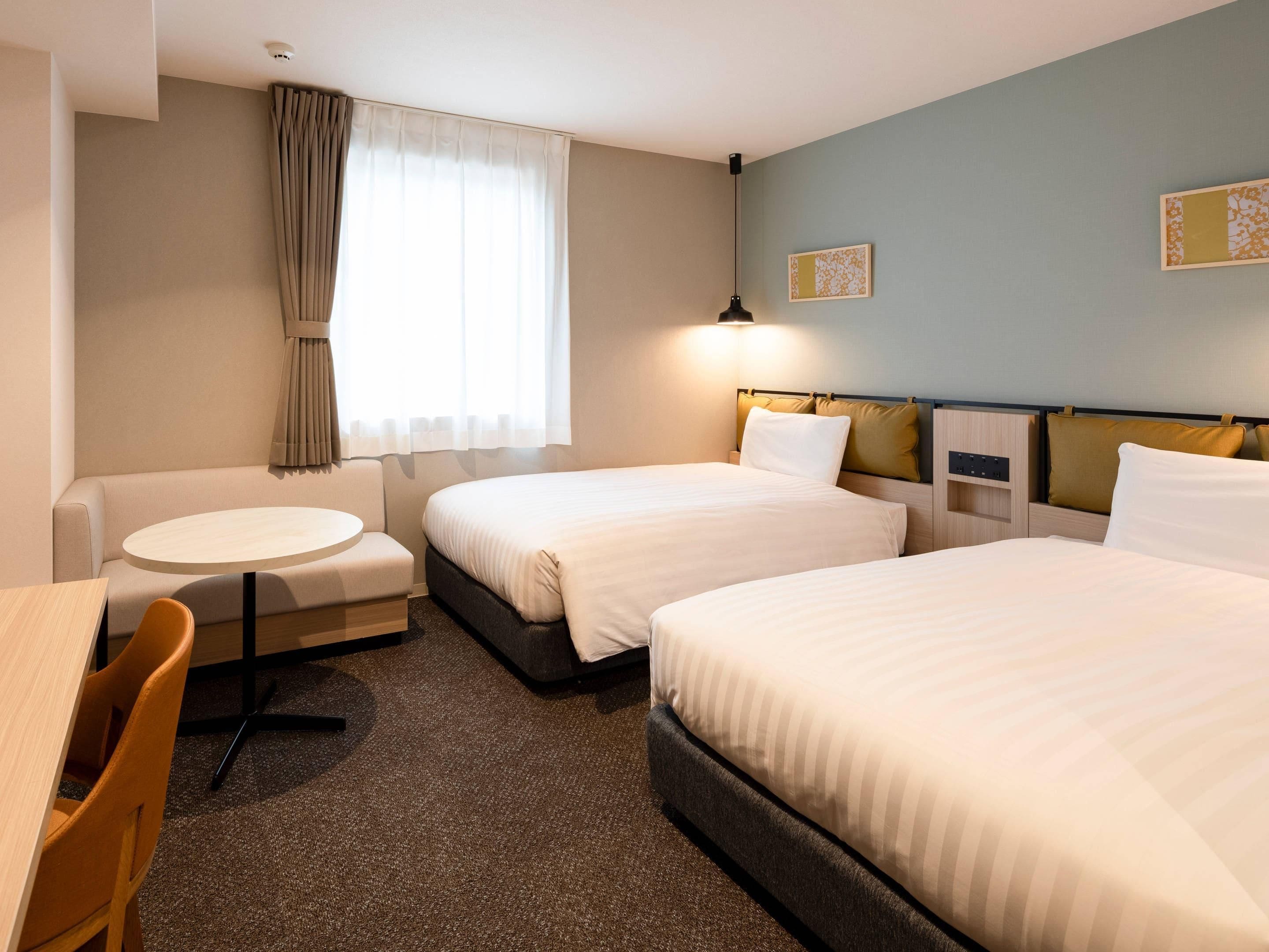 Camera d'albergo con due letti, un tavolo rotondo, una poltrona e una finestra con tende.