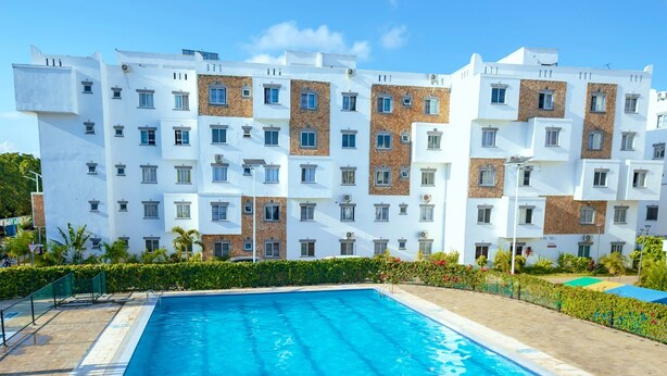 A swimming pool with clear blue water, surrounded by a white building with multiple windows and balconies.