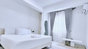 A white bedroom with a bed, a ceiling fan, a bedside table, and a large window with curtains.