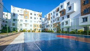 An outdoor basketball court adjacent to a multi-story residential building with a clear blue sky.