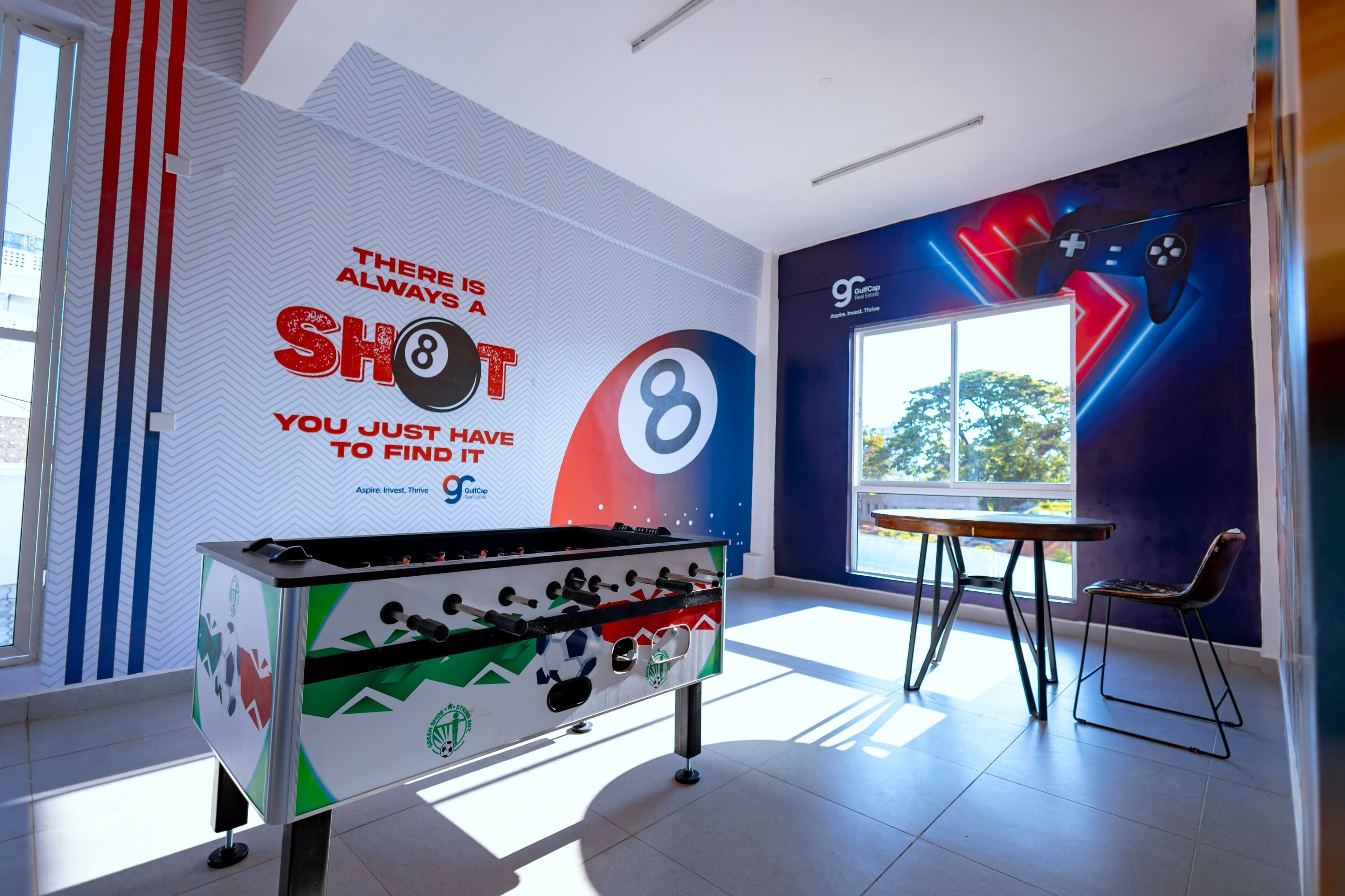 A foosball table in a brightly lit room with a motivational quote on the wall and a large window.