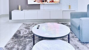 A modern living room with a flat-screen TV mounted on a white wall, a grey patterned sofa, and a round coffee table.