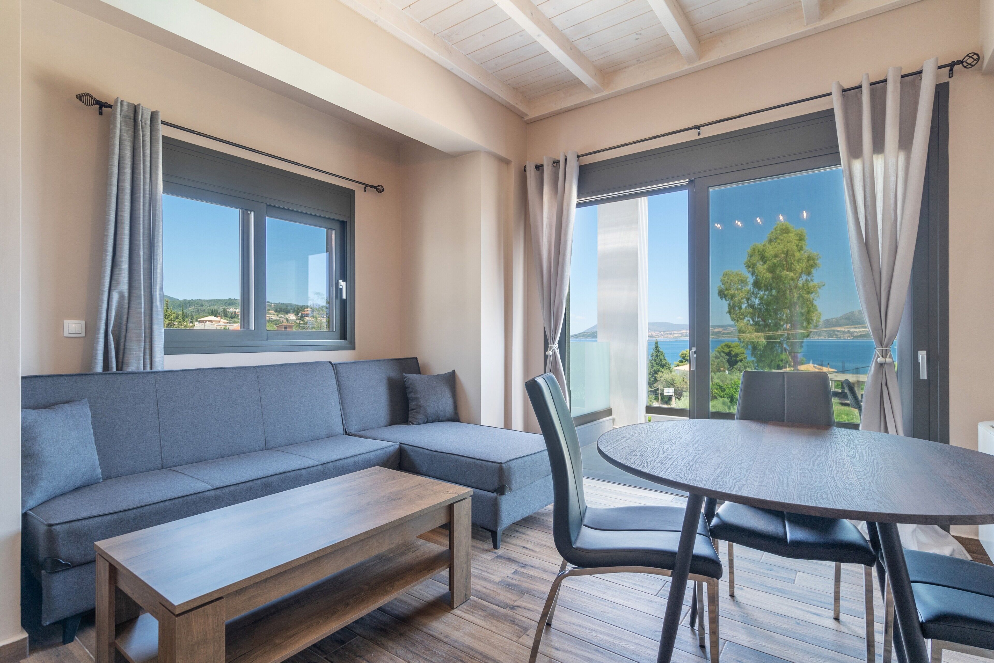 Un salon moderne avec un canapé, une table ronde et des chaises, de grandes fenêtres avec des rideaux et une vue sur la mer.