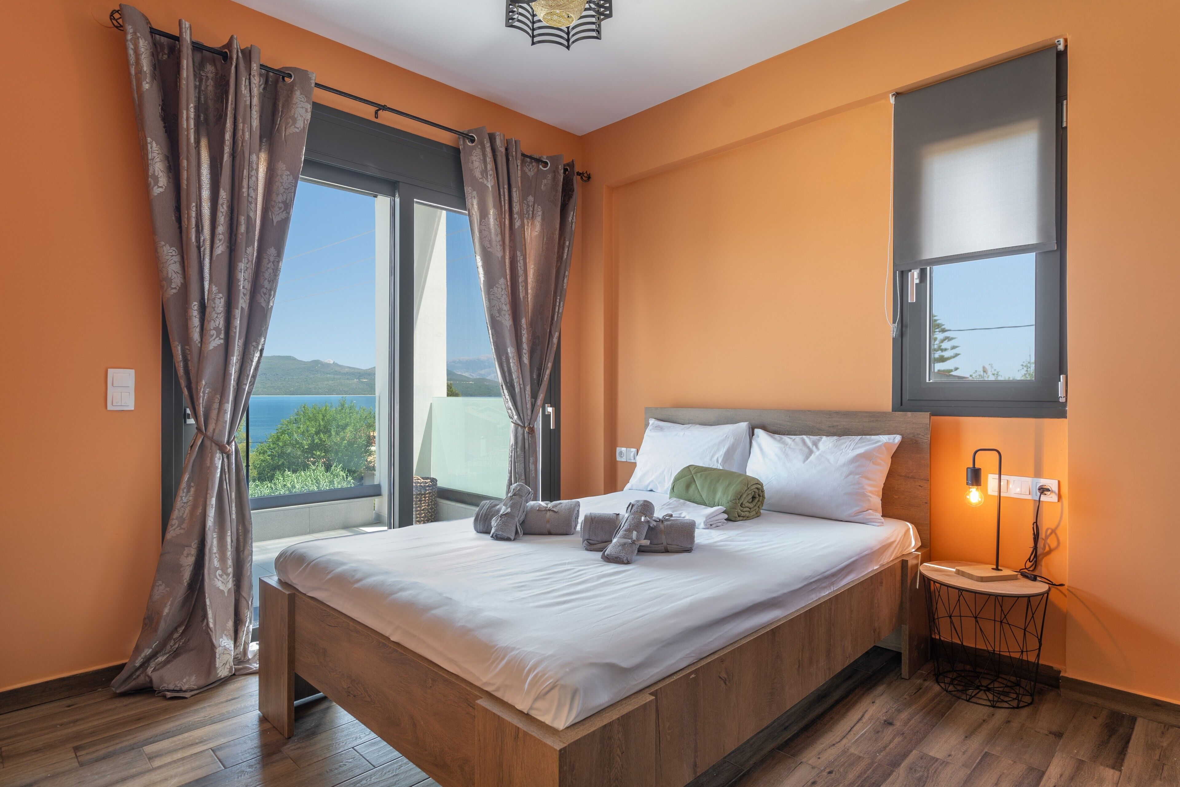 Une chambre à coucher avec un lit, des rideaux, une table de chevet avec une lampe et une vue sur l’extérieur.