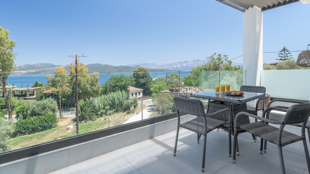 En balkon med et bord og stole, der udover et smukt landskab med bjerge og vand.