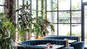 En moderne restaurant med blåt polstrede siddepladser, store vinduer og hængende papirlanterner.