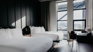 Et moderne hotelværelse med to senge, et skrivebord og udsigt over byen gennem store vinduer.