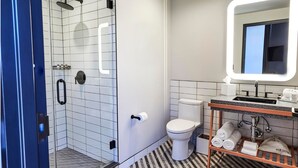 Et moderne badeværelse med et brusebad bag glas, et hvidt toilet, en vask med spejl og en håndklædestang.