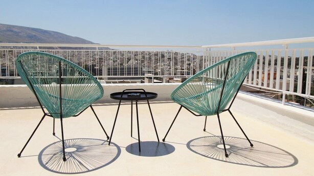 Une terrasse sur le toit avec deux chaises en fil de fer vert et une petite table ronde.