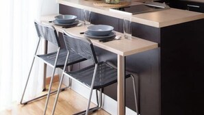 Une cuisine moderne avec un îlot central, des chaises noires, un luminaire suspendu et des armoires en bois.