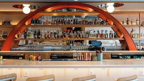 Un bar doté d’une arche en bois incurvée, de plusieurs étagères remplies de bouteilles et de trois tabourets.